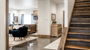 Un interior moderno con una escalera de madera, una cocina con armarios de madera y una sala de estar con un sofá oscuro y cortinas estampadas.