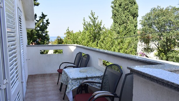 A balcony with a table and chairs, overlooking a scenic view of trees and the sea. - Apartment Tommy (Malinska-Dubasnica)