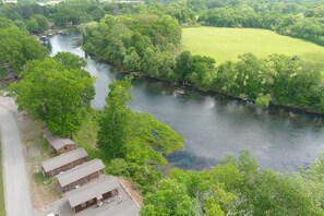 A riverside property with multiple cabins, a paved road, and lush greenery.