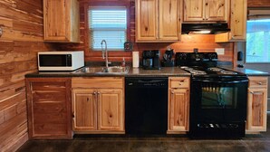 Una cocina con gabinetes de madera, microondas, lavavajillas, estufa y pileta.