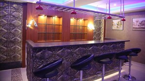 A bar area with a stone countertop, four bar stools, and a wooden cabinet with a glass door. - Hotel Venition Inn (Coimbatore)