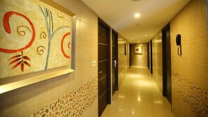 A hotel hallway with a modern design, featuring a large abstract painting on the wall, a phone on the wall, and a patterned floor. - Hotel Venition Inn (Coimbatore)