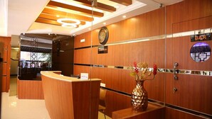 A reception area with a wooden reception desk, a clock, and a vase with flowers. - Hotel Venition Inn (Coimbatore)