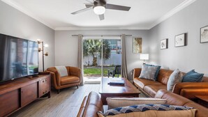 Ein modernes Wohnzimmer mit Ledersofas, einem Holztisch, einem Flachbildfernseher und einem Deckenventilator.