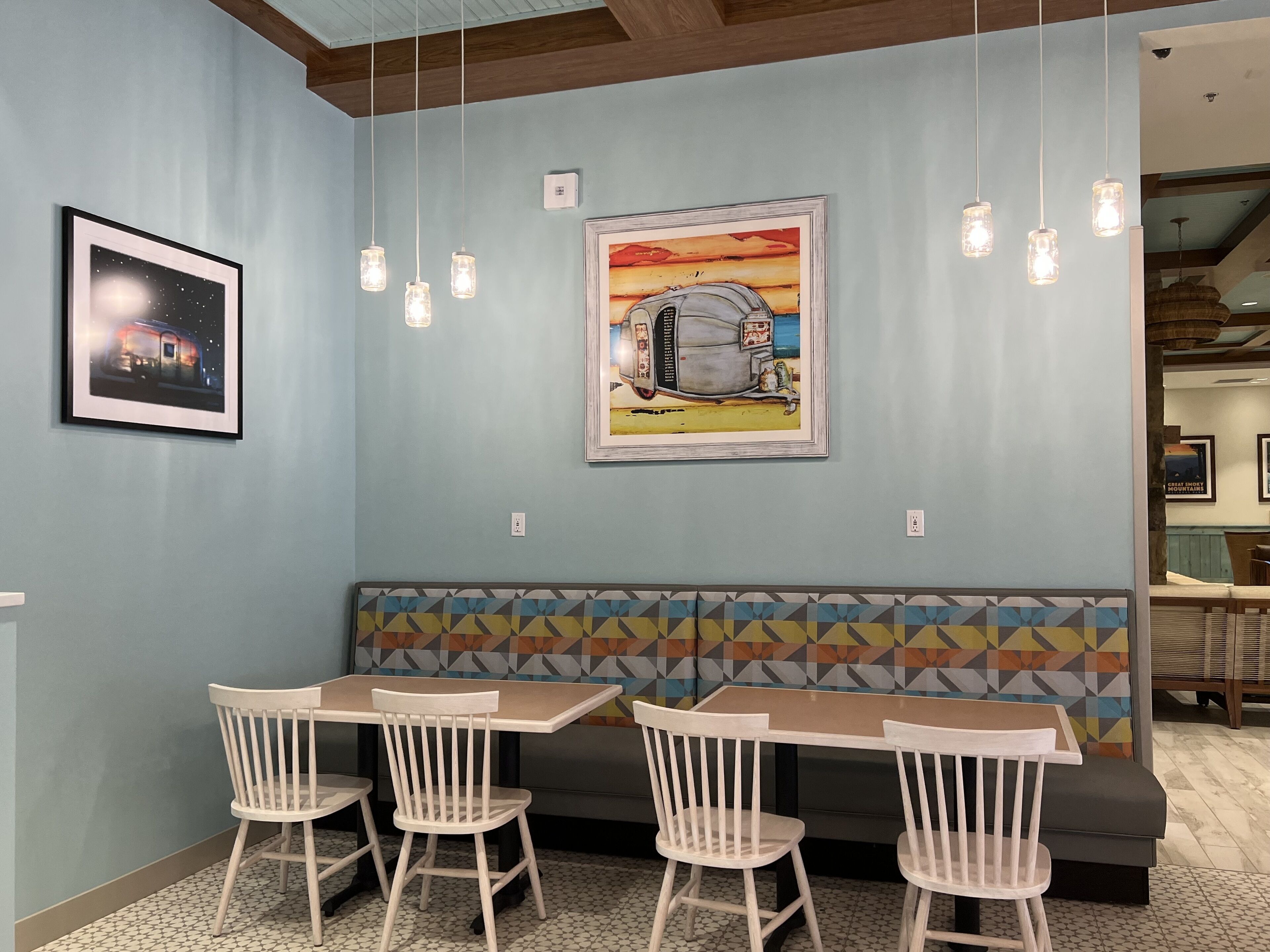 Interior de restaurante con zona de mesas tipo cabina, lámparas colgantes y cuadros en las paredes.