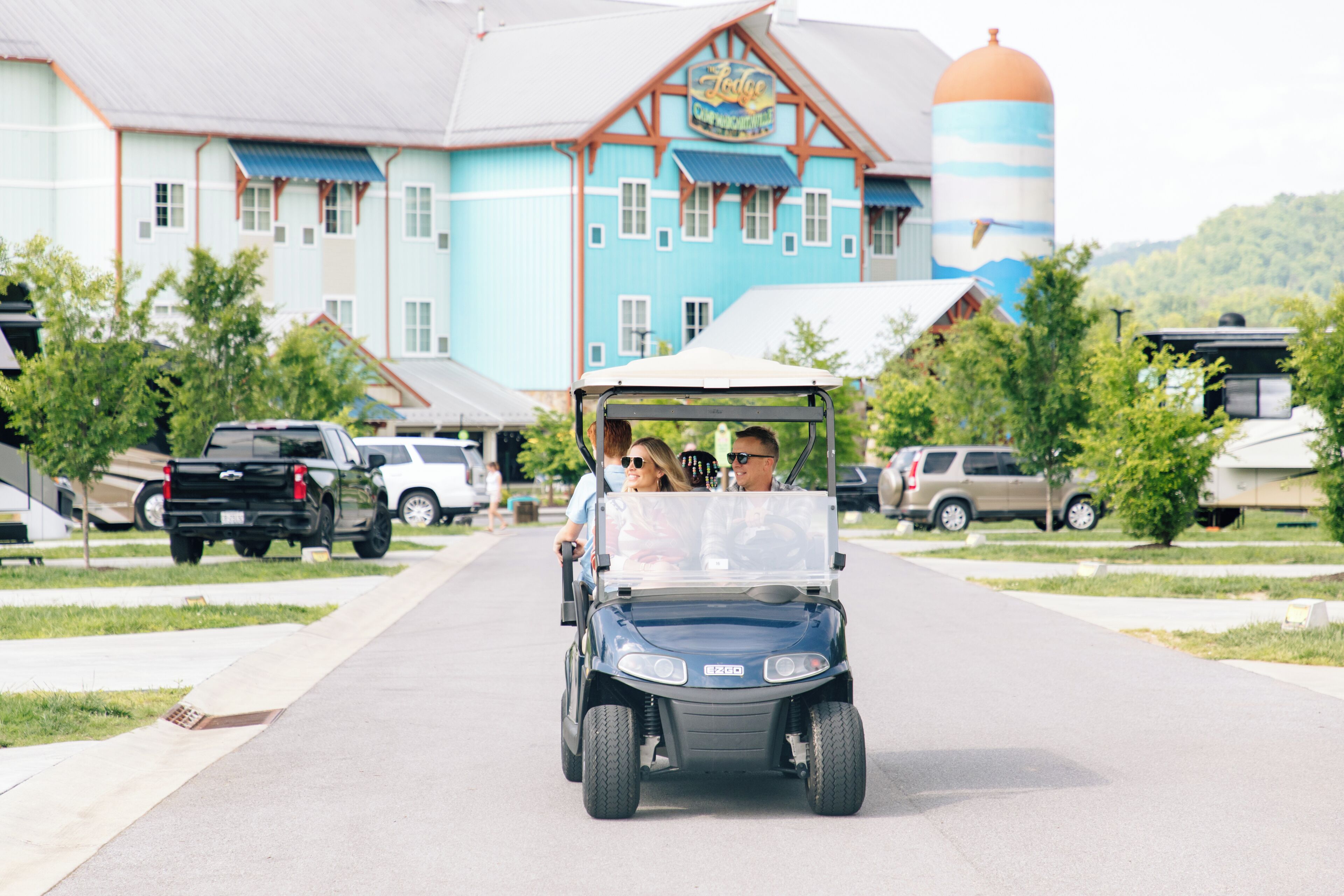 A golf cart on a paved path with a building featuring a blue facade and a large cylindrical structure in the background.