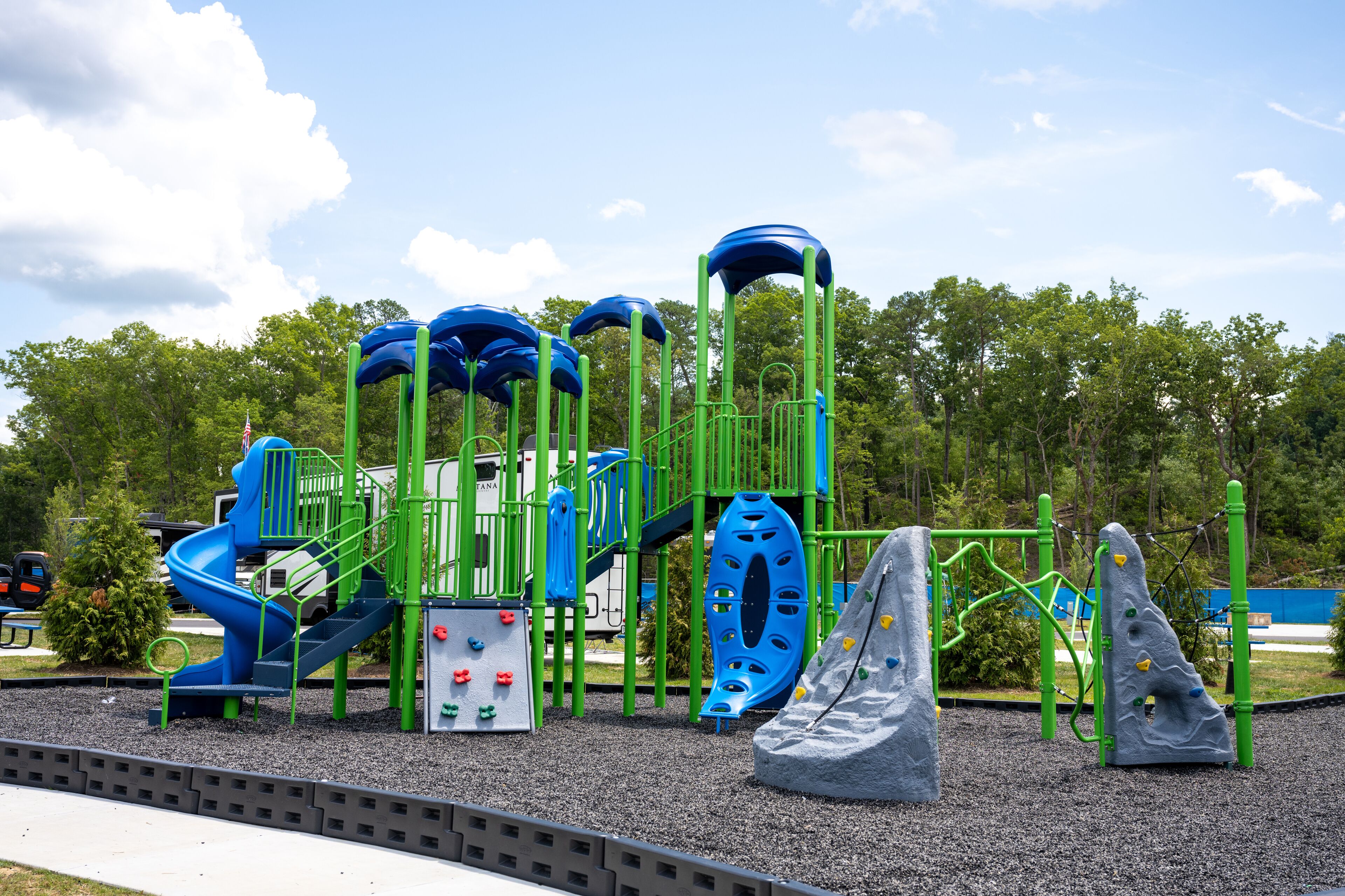 Une aire de jeux avec un toboggan bleu, des structures d’escalade et un mur d’escalade.