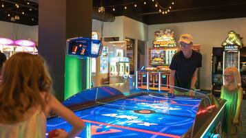 Un flipper dans une salle d’arcade lumineuse, avec des néons et divers jeux d’arcade en arrière-plan.