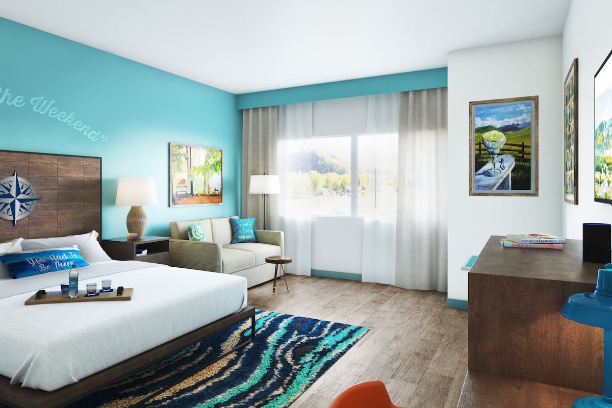 A hotel room with a large bed, a desk, a chair, a TV, and a window with curtains.