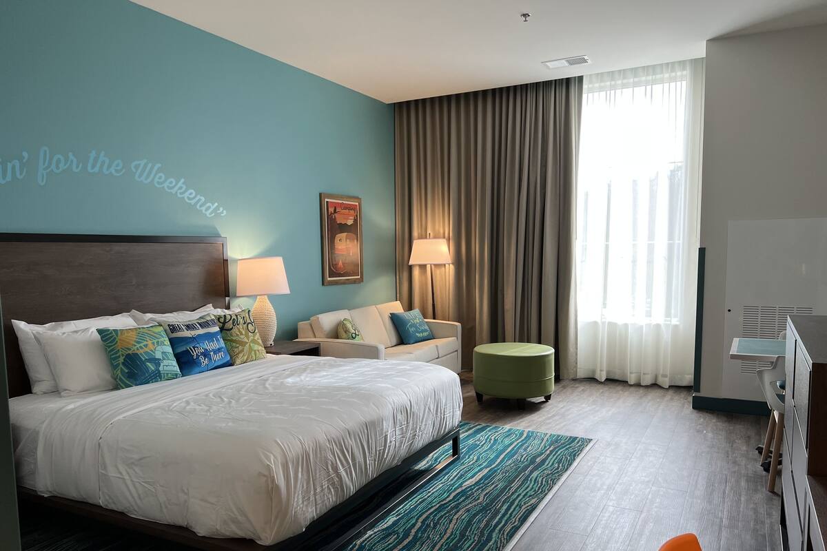 A hotel room with a bed, a sofa, a small ottoman, a desk, and a chair.