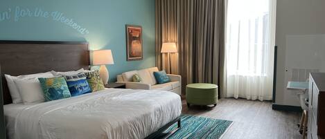 A hotel room with a bed, a sofa, a small ottoman, a desk, and a chair.