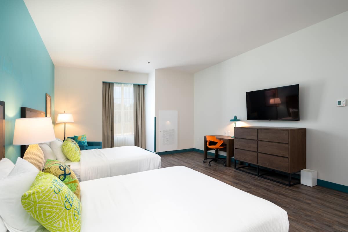 A hotel room with two beds, a desk, a chair, a TV, and a window with curtains.