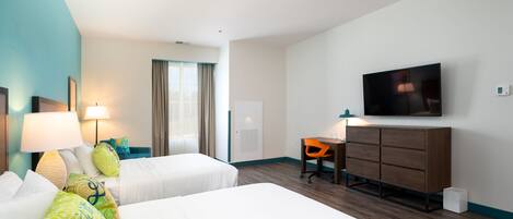 A hotel room with two beds, a desk, a chair, a TV, and a window with curtains.