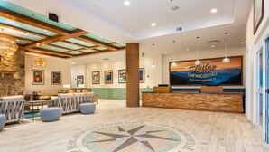 A spacious lobby with a wooden ceiling, a large reception desk, and a wall-mounted TV displaying 'Lodge Camp Margartaville'. - The Lodge at Camp Margaritaville (Pigeon Forge)