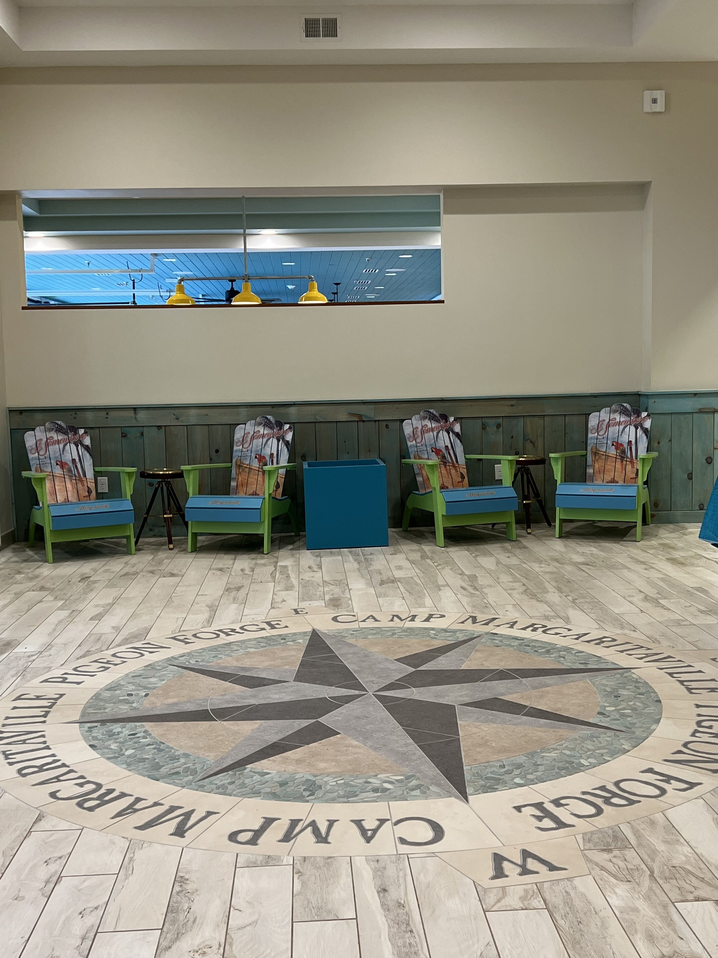 A room with a large window, wooden floor with a star design, green chairs, and a blue table.