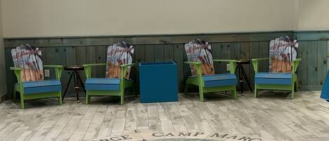 A room with a large window, wooden floor with a star design, green chairs, and a blue table.