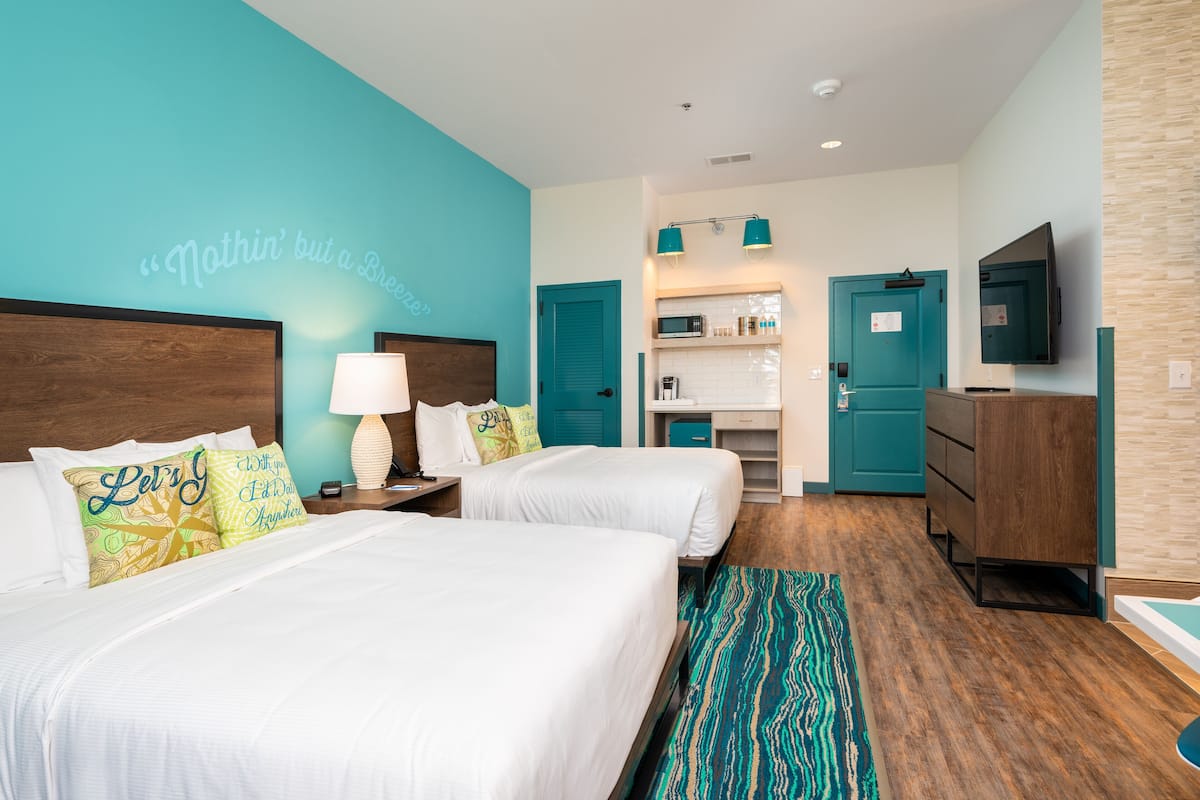 A hotel room with two beds, a kitchenette, a TV, and a bathroom.