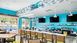 A bar with a blue wall, wooden tables and chairs, and a counter with a cash register. - The Lodge at Camp Margaritaville (Pigeon Forge)