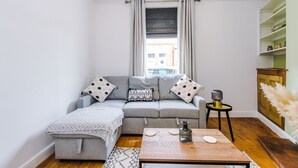A modern living room with a grey sofa, a small side table, a wooden coffee table, and a window with curtains.