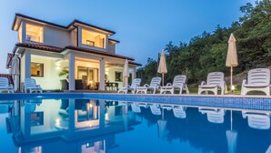 Ein zweistöckiges Haus mit Swimmingpool, Liegestühlen und Sonnenschirmen.