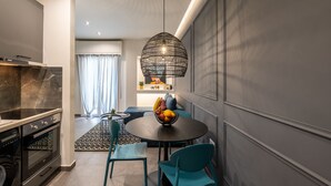 A modern kitchen with a built-in oven and a dining area with a round table and teal chairs. - Ports Crossroad E (Πειραιάς)