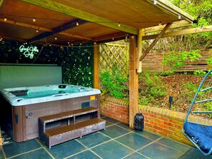 Un jacuzzi bajo una pérgola de madera con un fondo de pared verde y un letrero de neón.