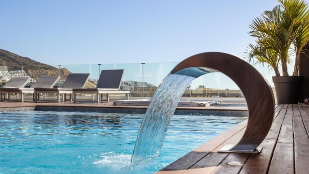 A pool with a wooden deck and lounge chairs.