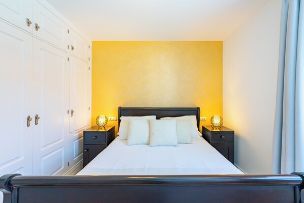 Une chambre d’hôtel avec un lit, deux tables de chevet, une armoire et un mur jaune.