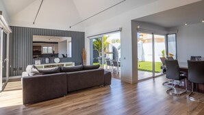 A modern living room with a grey sectional sofa, wooden flooring, and a view of a kitchen and outdoor patio.