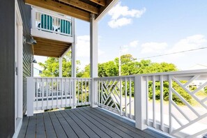 Eine Holzterrasse mit weißen Geländern, ein Balkon im zweiten Stock mit grünen Fensterläden und freier Sicht auf die umliegende Grünfläche.