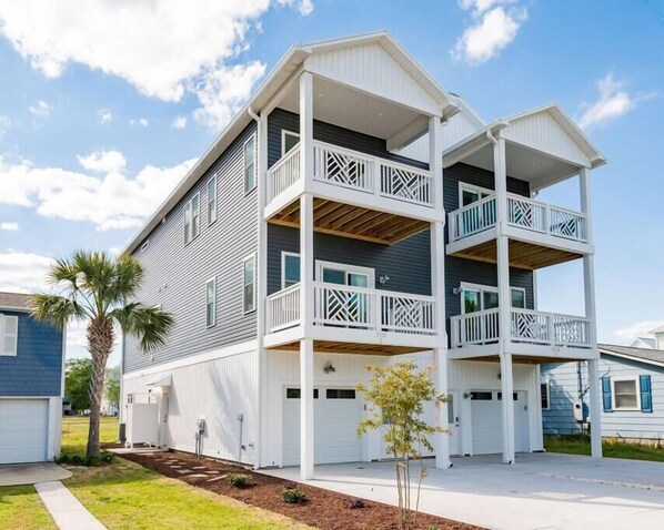 A two-story building with balconies, a garage, and a small tree in the front yard.