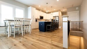A modern kitchen with white cabinets, a central island, and a dining area with white chairs. - Three Seas at the B, Walk to Tiki Bar and Beach (Carolina Beach)