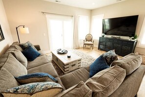 Ein Wohnzimmer mit einer Couch, Sesseln, einem Couchtisch, einem Fernseher und einem Schrank.