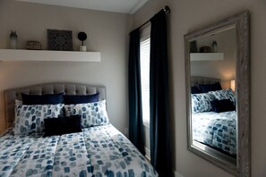 A bedroom with a bed, a mirror, and a window with curtains.