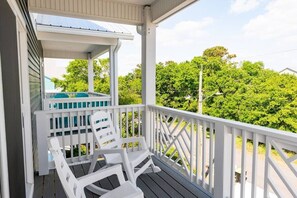 A covered porch with white railings and two white chairs.
