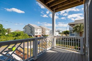 A wooden deck with a white railing overlooking a residential area with houses and a clear sky.