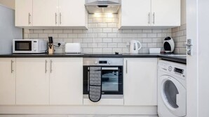 A compact kitchen with white cabinets, a microwave, toaster, kettle, oven, and a washing machine. - Homely Spaces Apt A, Large Studio W/king, 2guests (Bedford)