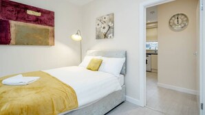 A modern bedroom with a bed, a bedside lamp, and a door leading to a kitchen. - Homely Spaces Apt A, Large Studio W/king, 2guests (Bedford)