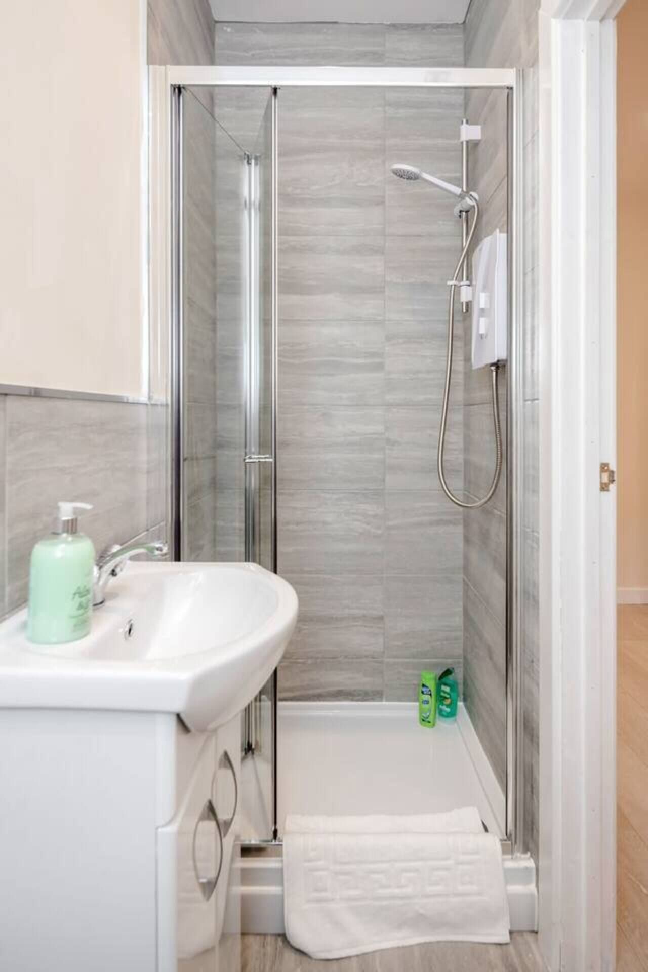 A modern bathroom with a glass shower enclosure, a white sink, and a small towel rack.