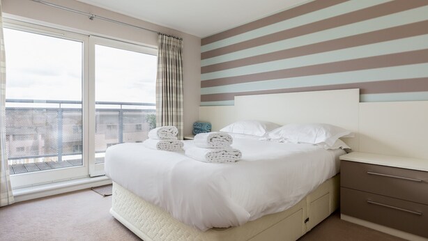 Una habitación de hotel con una cama grande, vistas al balcón y paredes a rayas.