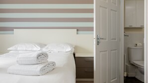 Una habitación de hotel con una cama, ropa de cama blanca, una pared a rayas y un baño visible a través de una puerta abierta.