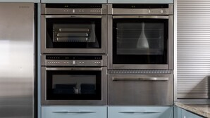 Cocina de acero inoxidable con tres hornos, un microondas y una campana extractora integrada.