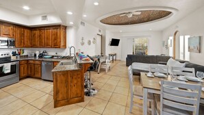 A spacious kitchen with wooden cabinets, a dining area with a table set for two, and a living room with a sofa and TV. - Luxury 2BR Beach Views Tennis Swim-Up Bar A205 (Puerto Peñasco)