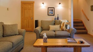 A living room with a wooden door, two sofas, a coffee table, a framed picture, and a staircase. - Elk Lodge: Spacious Cabin Near Trails & Ski Access (Winthrop)
