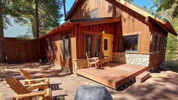 Una cabaña de madera con un porche, mobiliario exterior y una pared de piedra.