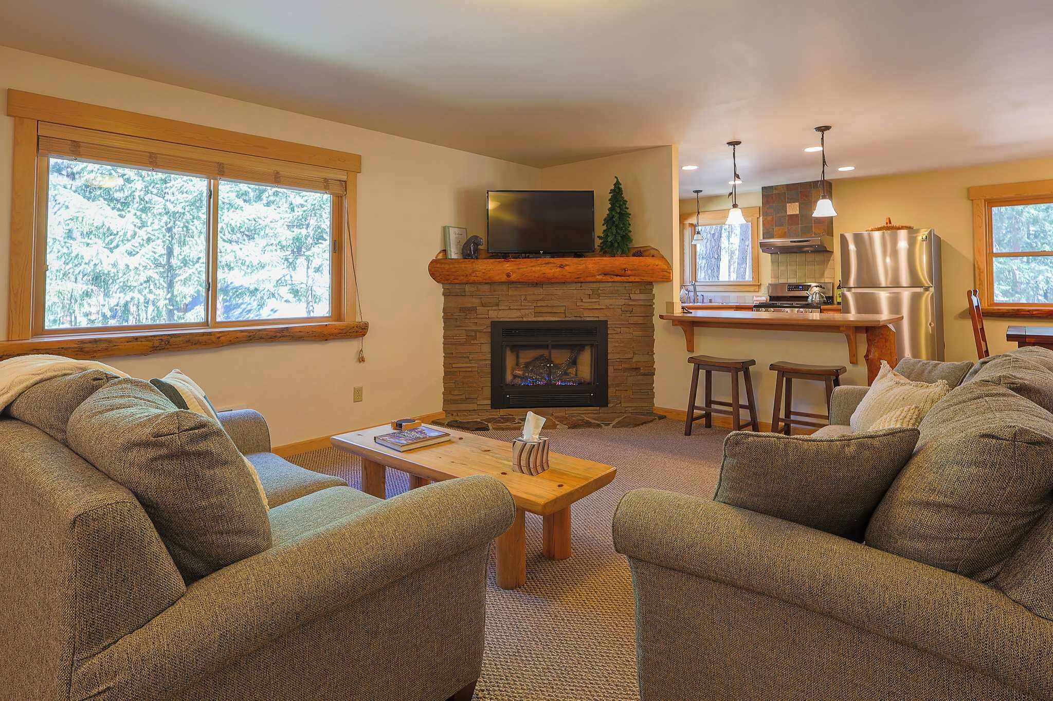 Una sala de estar con chimenea, televisión y una zona de cocina con taburetes de bar.