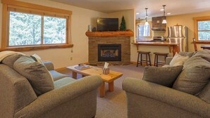 A living room with a fireplace, a television, and a kitchen area with bar stools. - Elk Lodge: Spacious Cabin Near Trails & Ski Access (Winthrop)