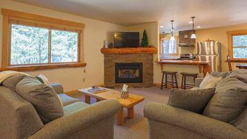 Una sala de estar con chimenea, televisión y una zona de cocina con taburetes de bar.
