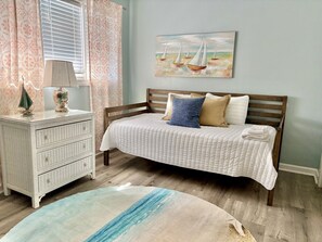 Une chambre à coucher avec un lit, une commode, une lampe et un tableau au mur.