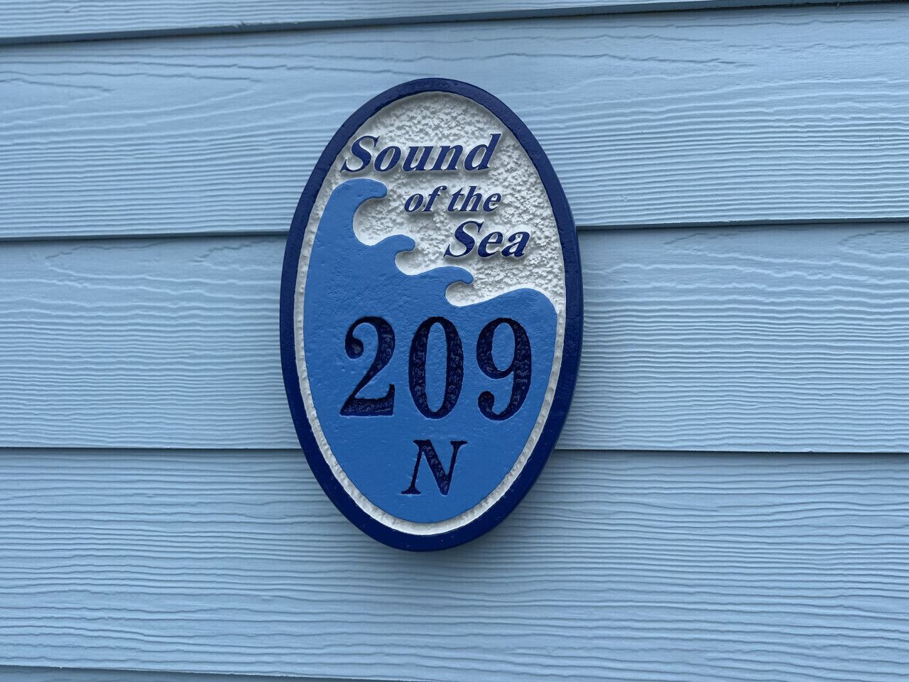 Un panneau indiquant le numéro de la maison, avec le texte « Sound of the Sea » et le numéro « 209 N », le tout sur un fond bleu.
